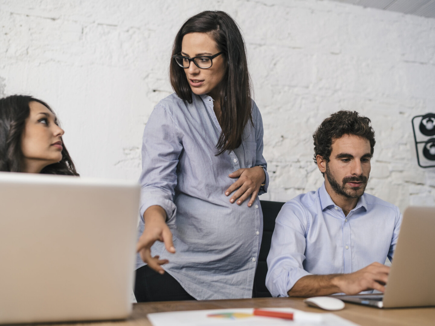 Creative people doing a brainstorming meeting in a modern studio with one of the employees being pregnant