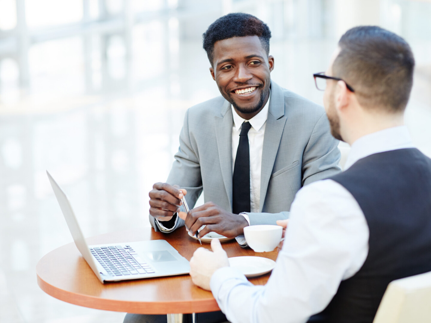 Portrait of successful African-American businessman smiling while discussing deal with Caucasian partner during meeting at coffee break to represent Benefits of Employee Wellness Programs article.